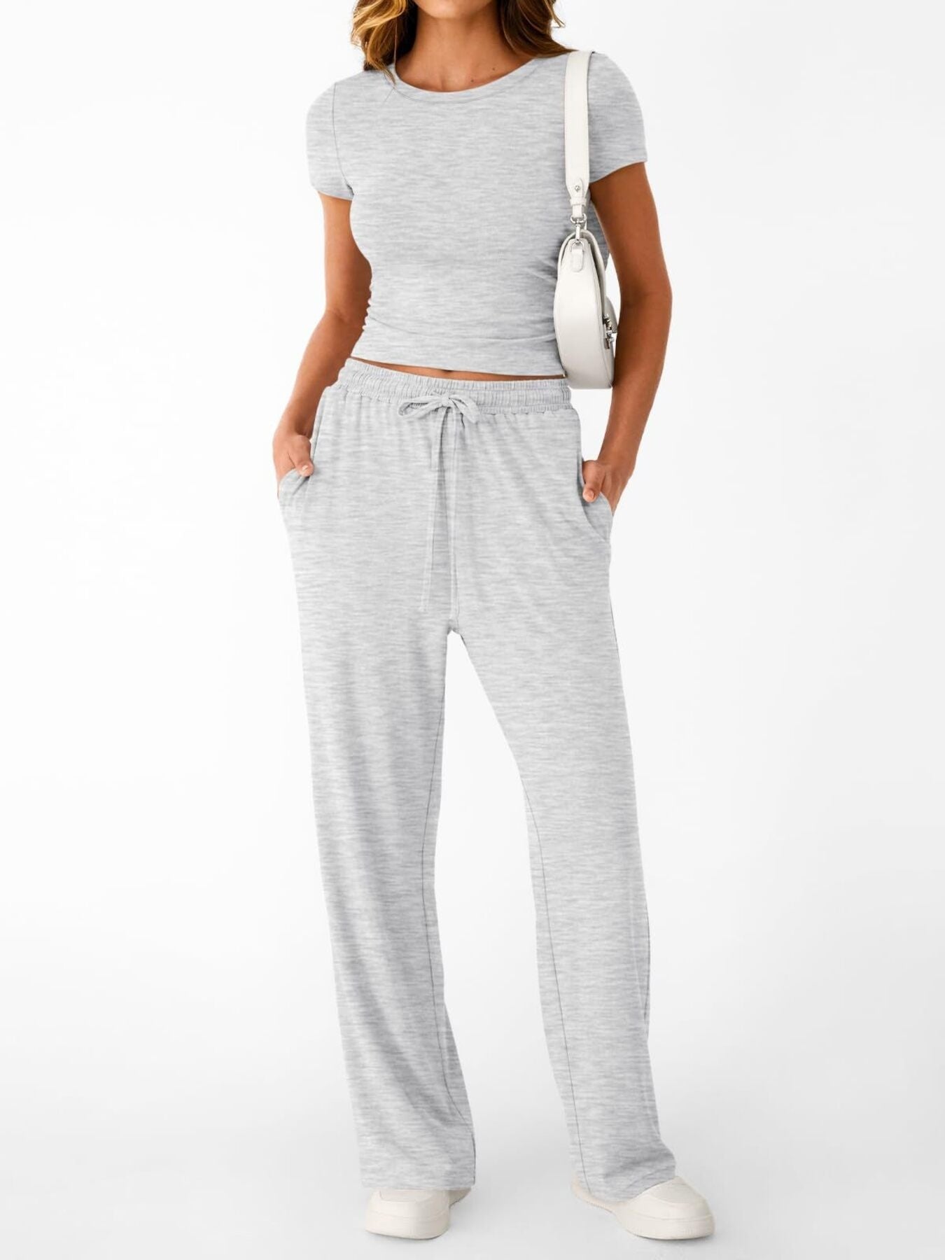 NEWYORKLISTED COMFORT COLLECTION: Woman wearing a gray crop top and pants with a white bag on a white background