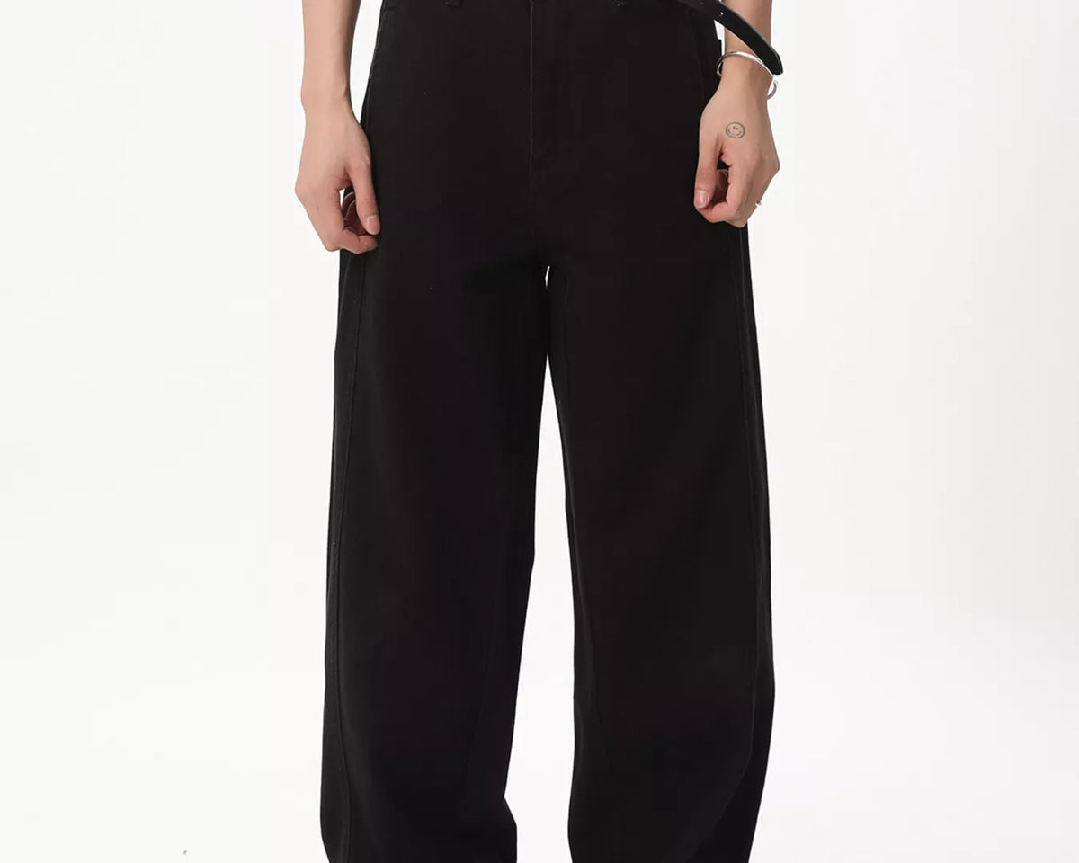 NEWYORKLISTED ATLAS MEN'S COLLECTION: A model wearing black wide-leg trousers with a black belt, paired with a cream graphic t-shirt and black shoes, photographed against a solid white studio background.