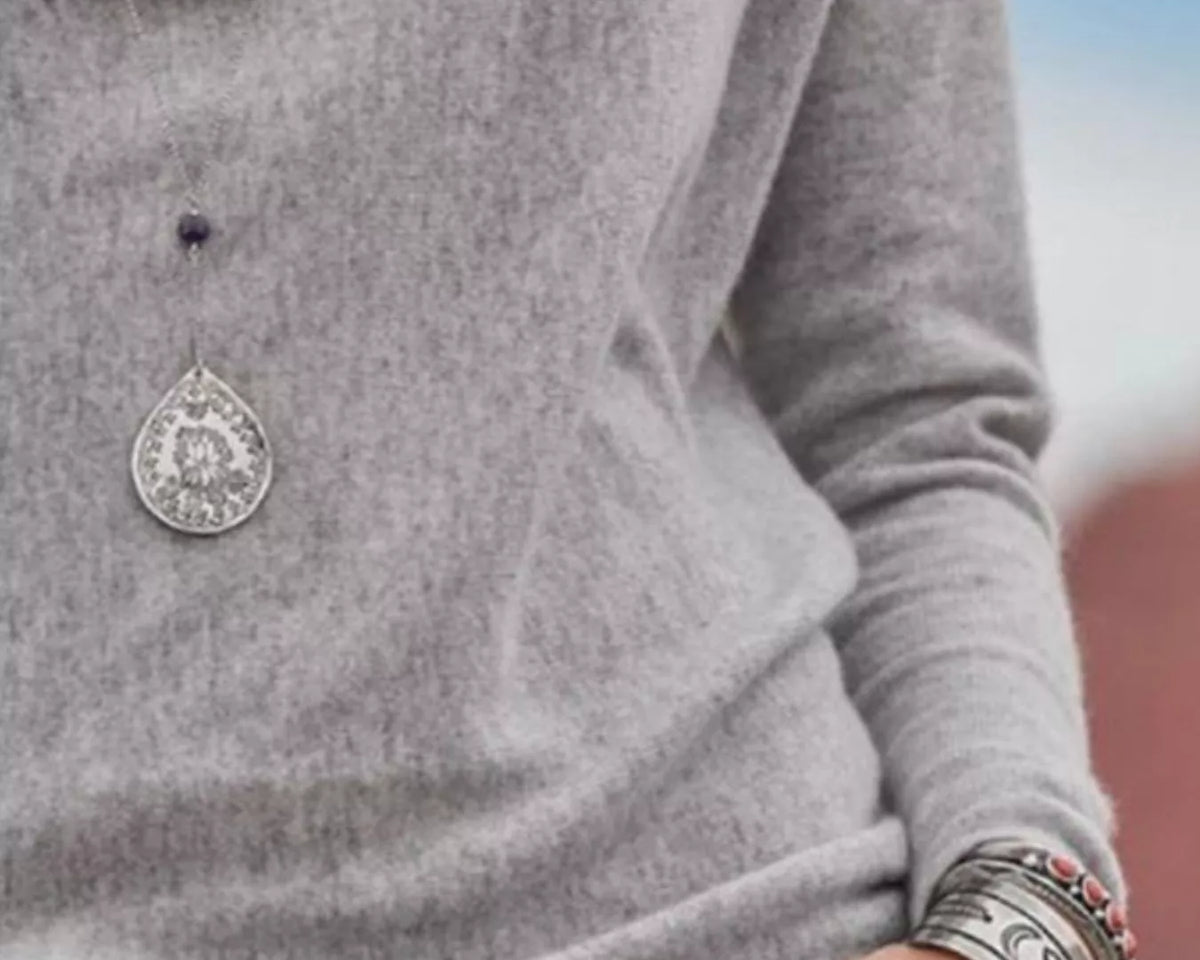 NEWYORKLISTED STYLE COLLECTION: Gray sweater with a decorative button and silver bracelet on a blurred background