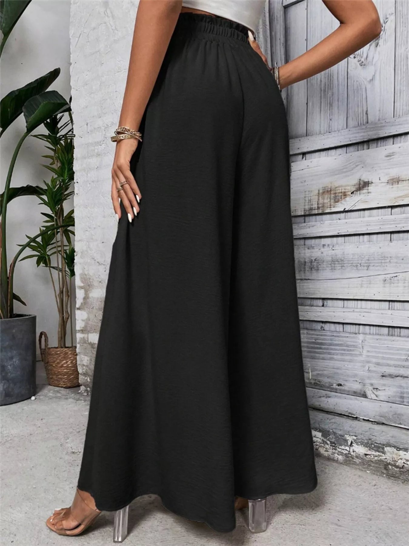 NEWYORKLISTED STYLE COLLECTION: Person wearing black wide-leg pants standing against a wooden wall.