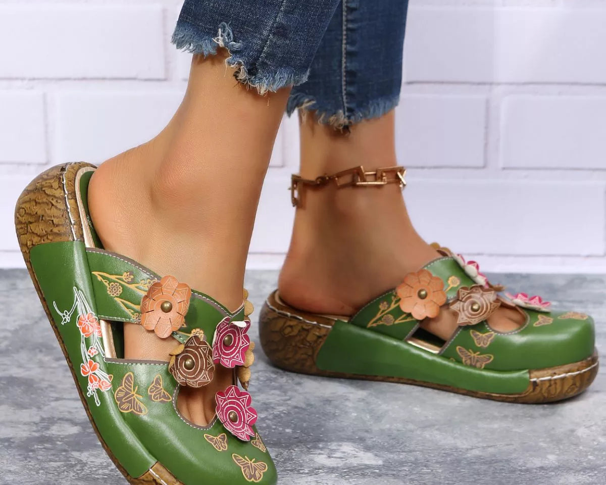 NEWYORKLISTED SHOE COLLECTION: Green clogs with floral designs worn by a person on a gray floor.