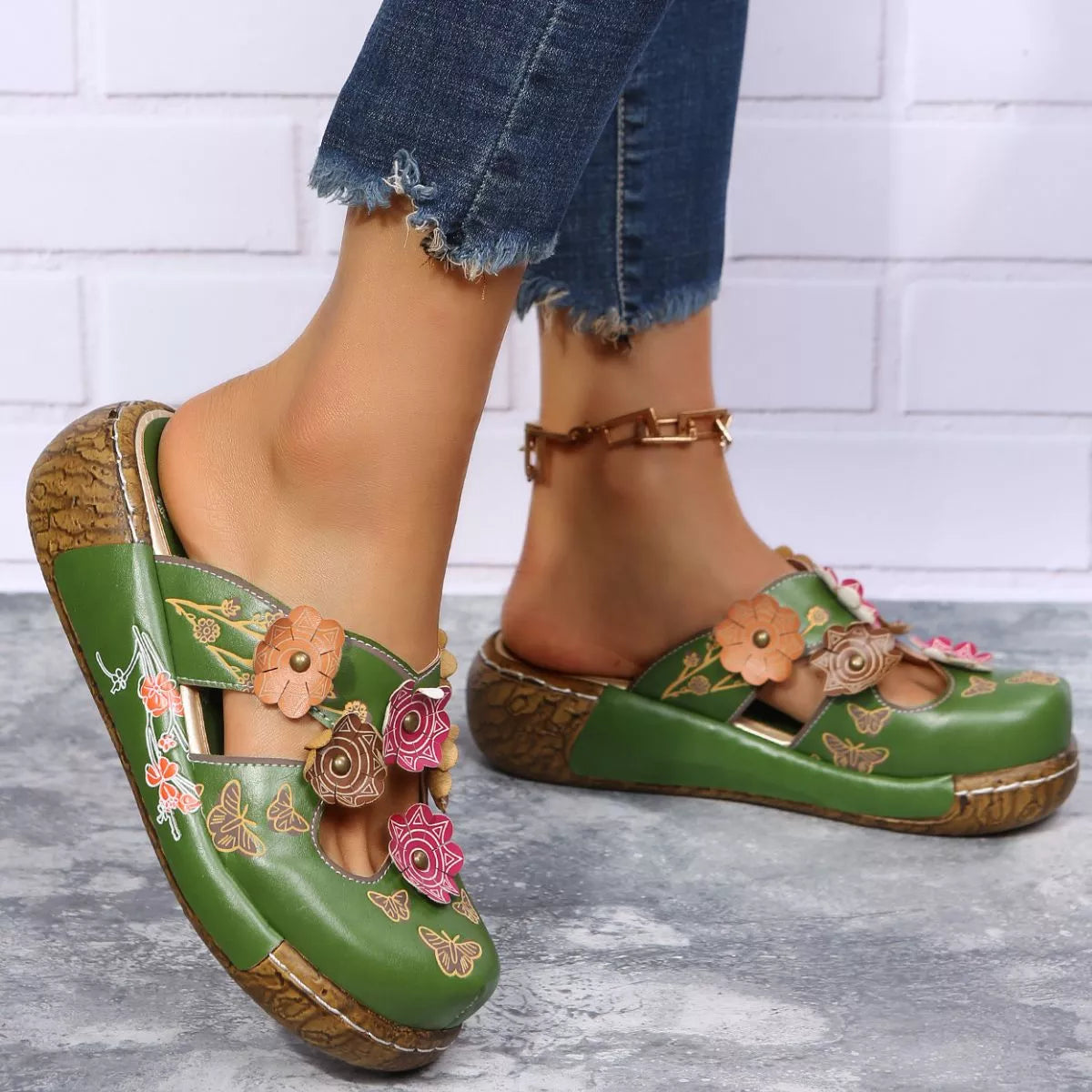 NEWYORKLISTED SHOE COLLECTION: Green clogs with floral designs worn by a person on a gray floor.