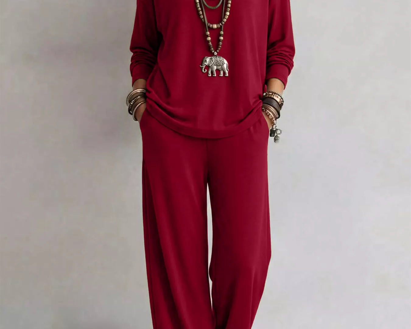 NEWYORKLISTED STYLE COLLECTION: A woman modeling a matching deep red long-sleeve top and wide-leg pants set, accessorized with layered silver necklaces, bracelets, and sandals, against a plain light gray background.