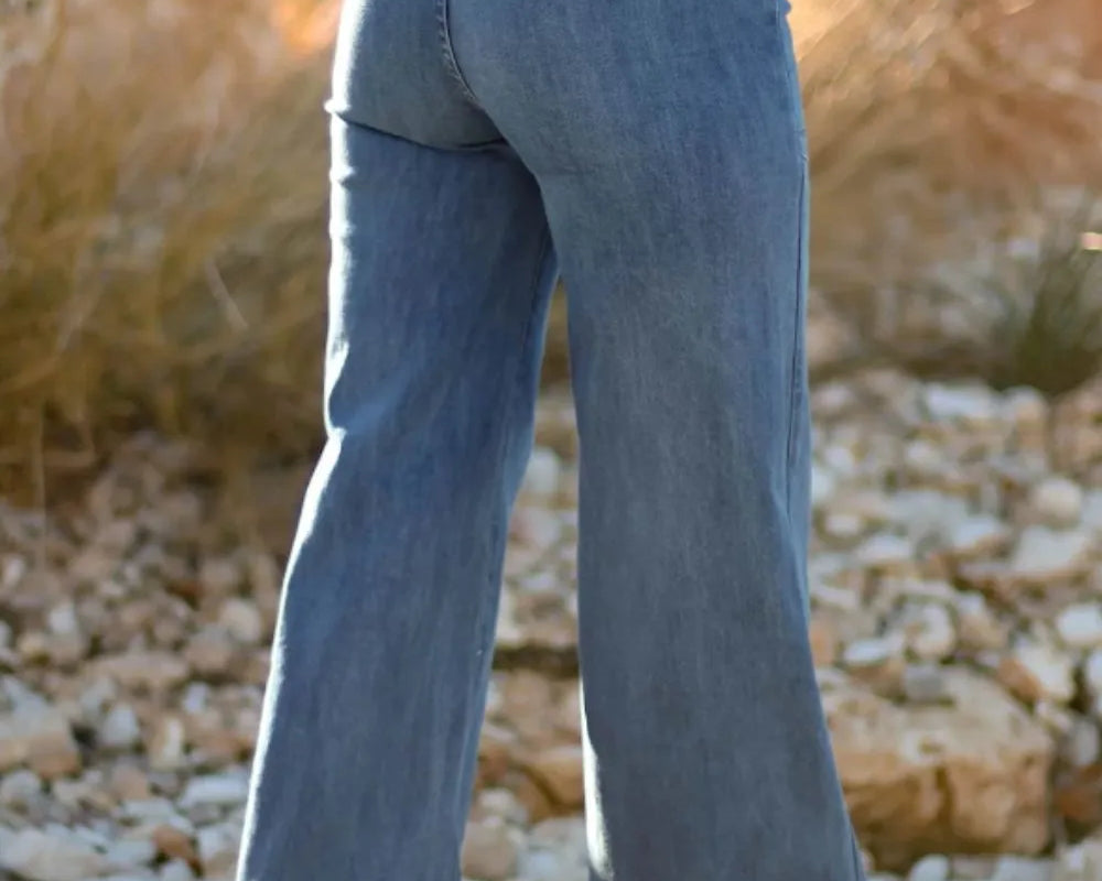 NEWYORKLISTED STYLE COLLECTION: Person wearing blue flared jeans standing on a rocky surface with a blurred natural background