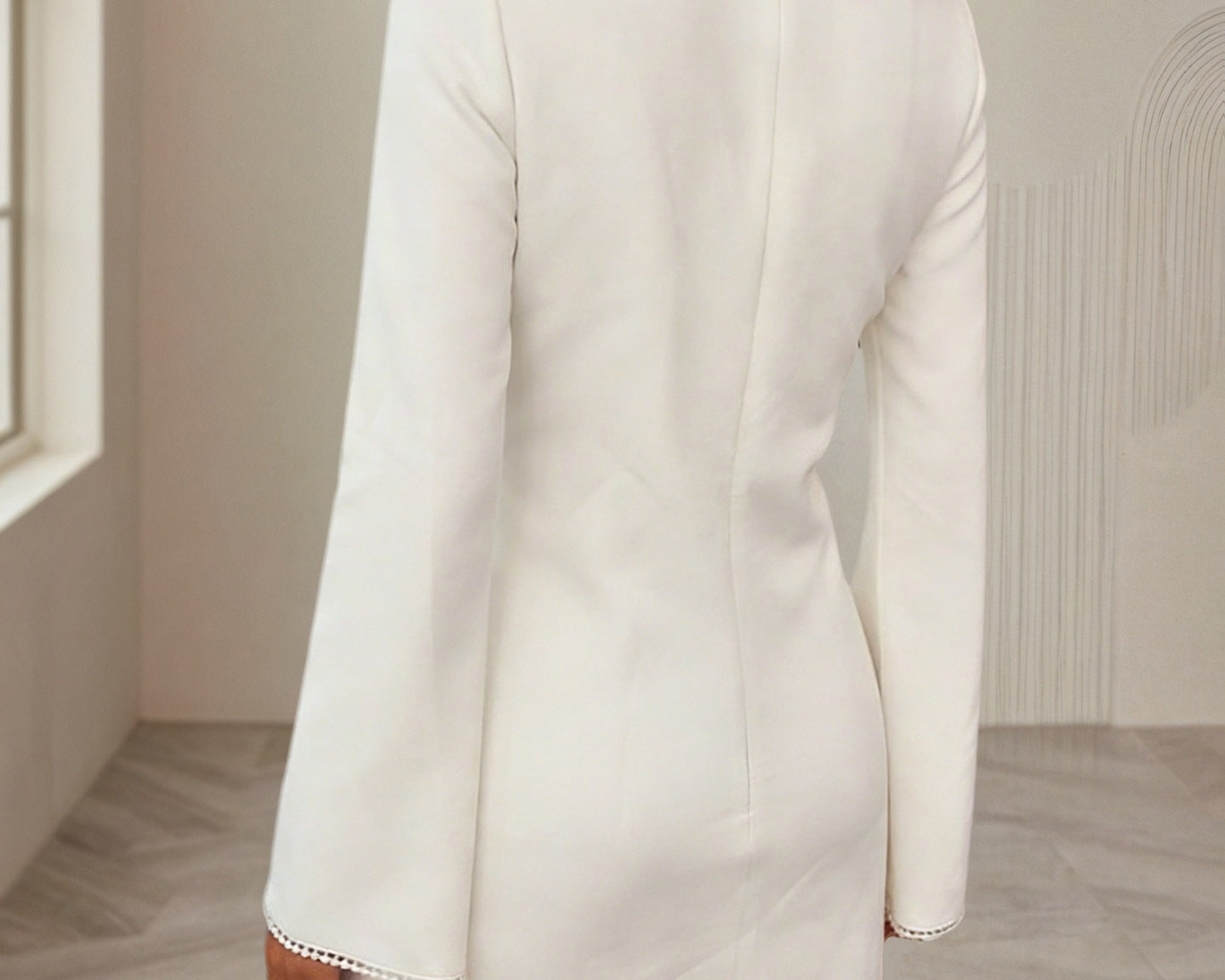 NEWYORKLISTED STYLE COLLECTION: White dress with long sleeves and trim details worn by a person in a neutral setting.