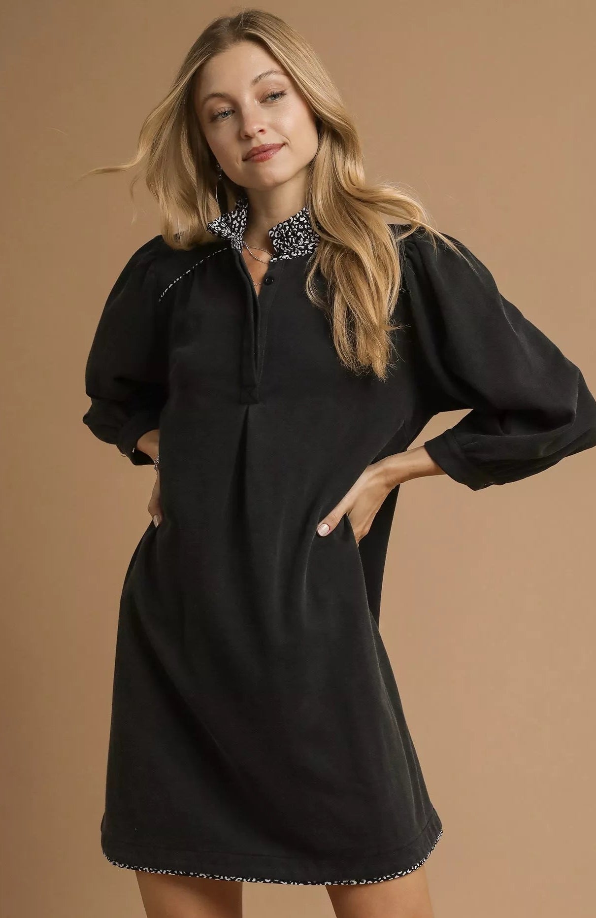NEWYORKLISTED STYLE COLLECTION: Woman wearing a black dress with puffed sleeves on a brown background