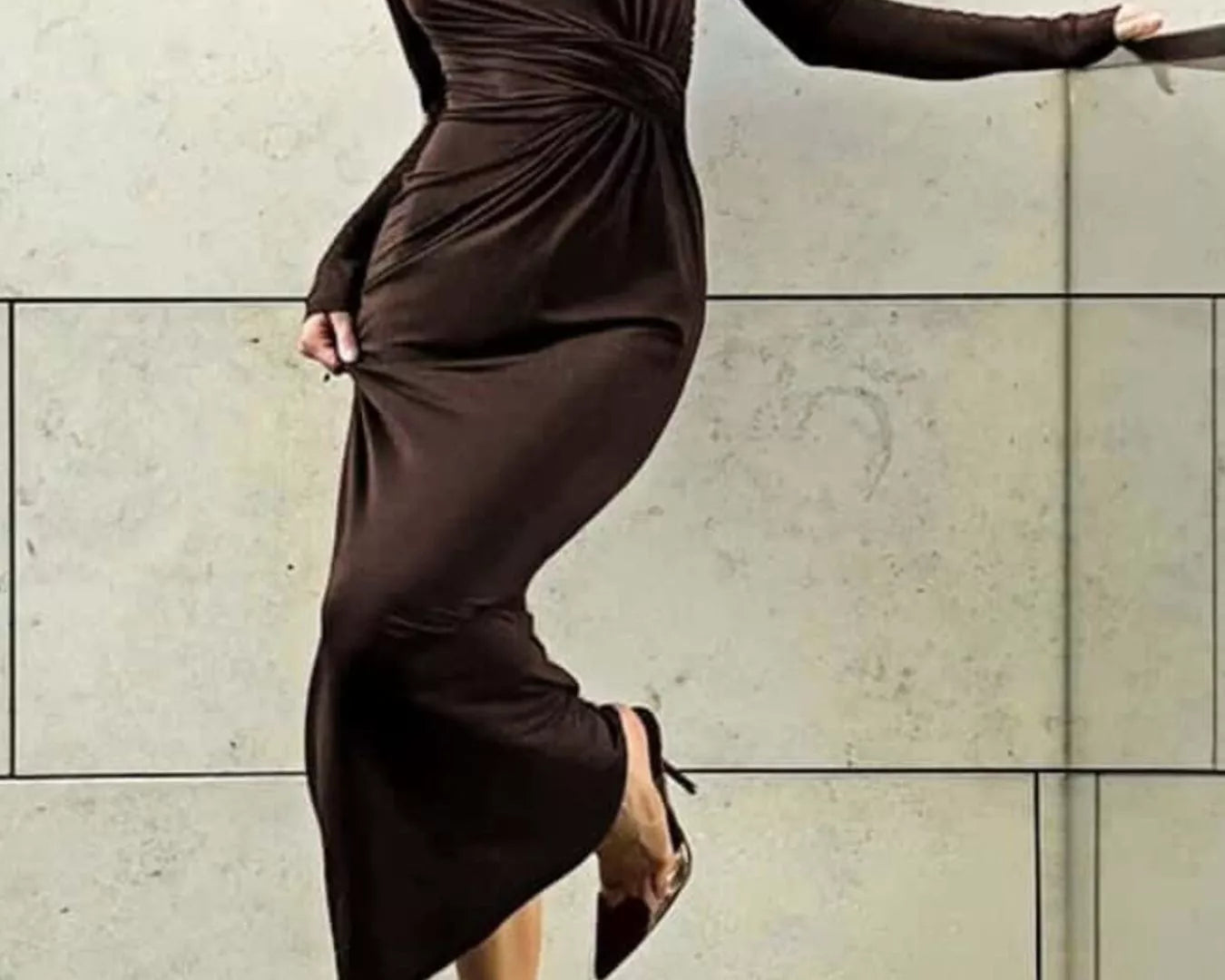 NEWYORKLISTED STYLE COLLECTION: Woman wearing a brown dress against a light-colored wall.