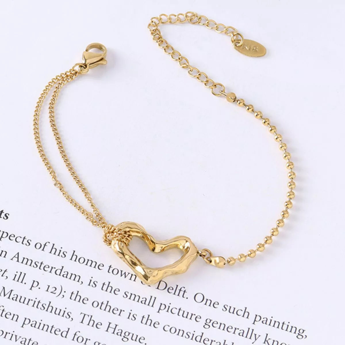 NYLD Glamour Collection by NEWYORKLISTED: Gold bracelet with a heart-shaped clasp on a white background