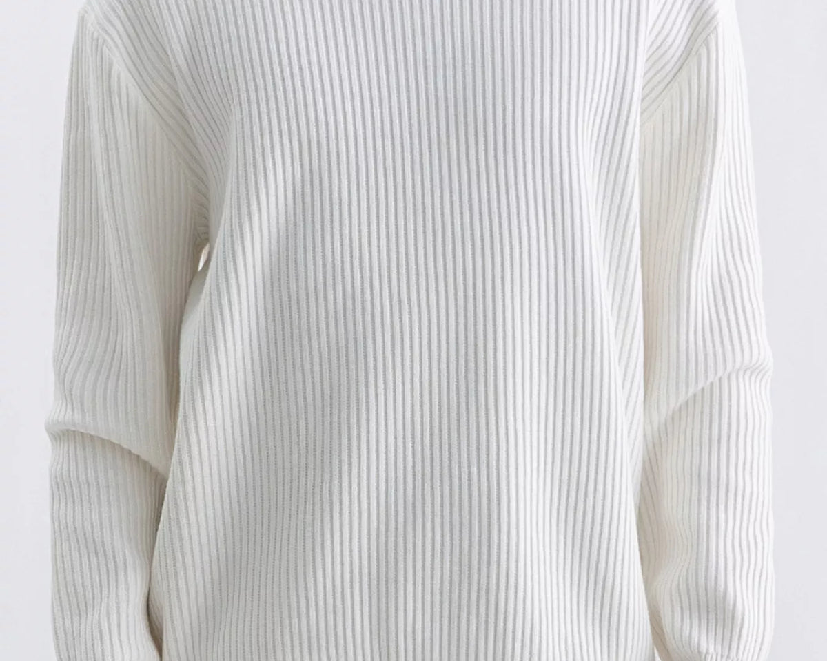 NEWYORKLISTED ATLAS MEN'S COLLECTION: A person wearing a ribbed long-sleeve crewneck sweater in off-white, paired with tan pants and a silver necklace, against a plain light background.