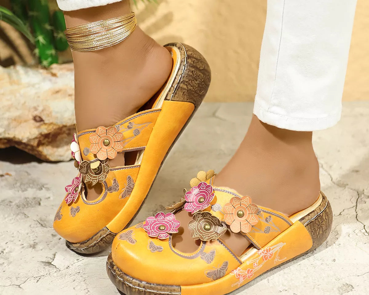 NEWYORKLISTED SHOE COLLECTION: Yellow sandals with floral designs worn by a person on a stone surface.