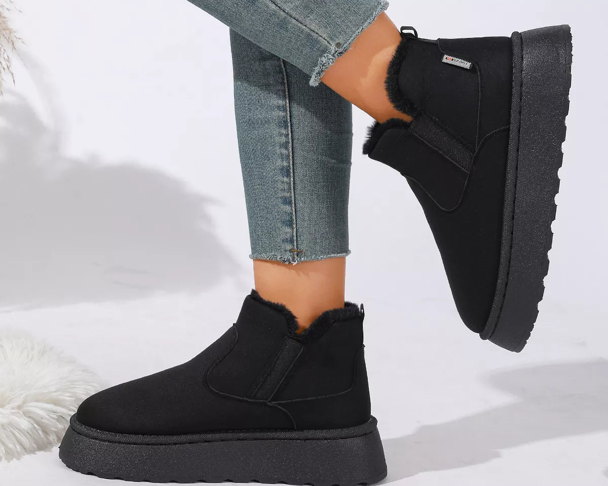 NEWYORKLISTED SHOE COLLECTION: A person wearing black ankle-height platform slipper boots with faux-fur trim, paired with blue jeans, shown against a clean white studio background.