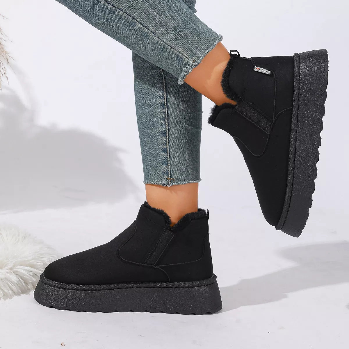 NEWYORKLISTED SHOE COLLECTION: A person wearing black ankle-height platform slipper boots with faux-fur trim, paired with blue jeans, shown against a clean white studio background.