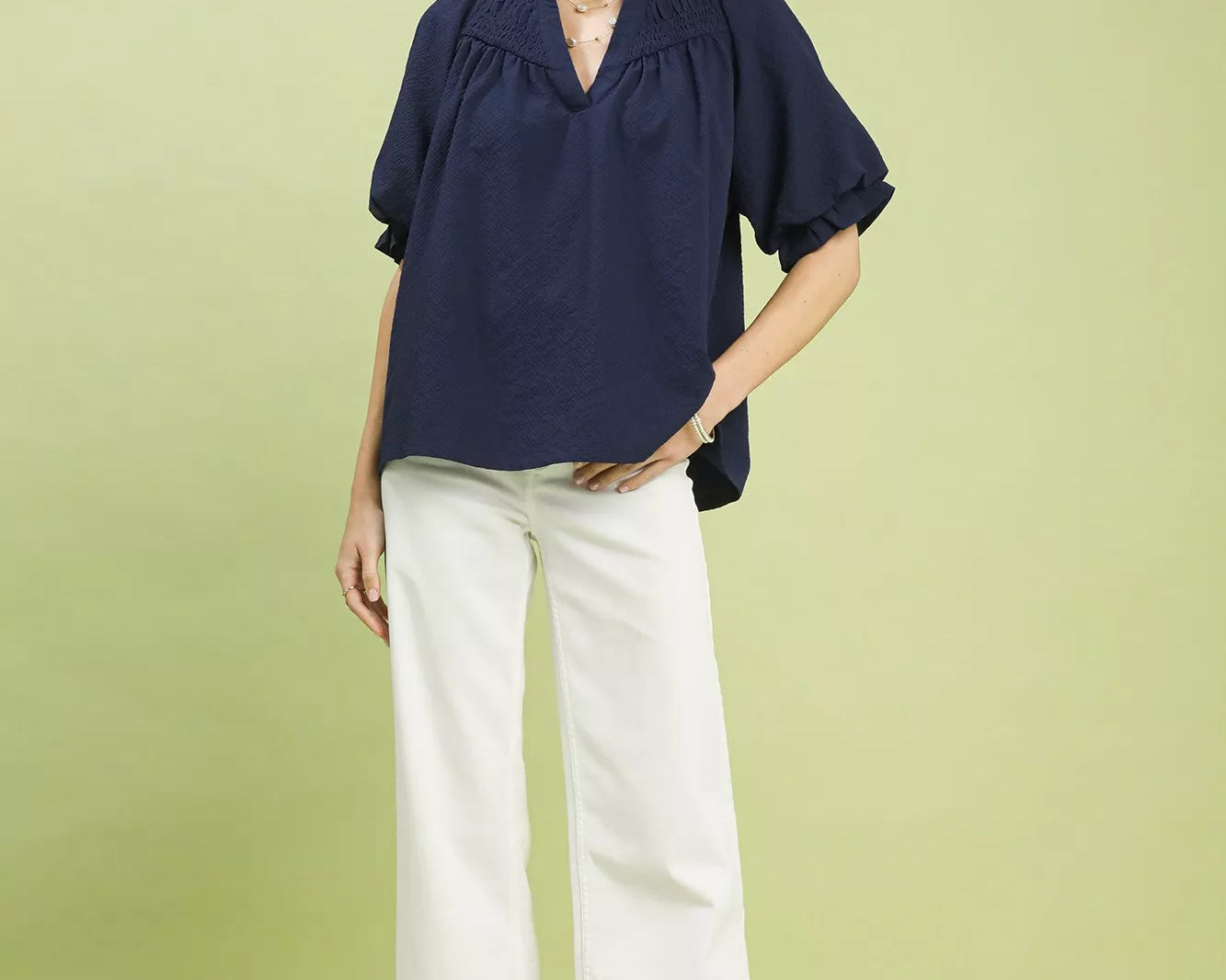 NEWYORKLISTED STYLE COLLECTION: Woman wearing a navy blouse and white pants on a light green background