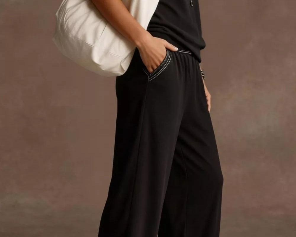 NEWYORKLISTED STYLE COLLECTION: Person wearing a black outfit with a white bag against a neutral background
