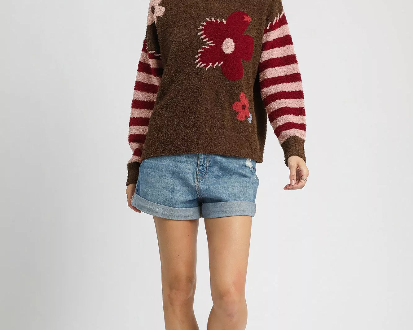 Woman wearing a brown sweater with floral designs and denim shorts on a white background: NEWYORKLISTED.COM