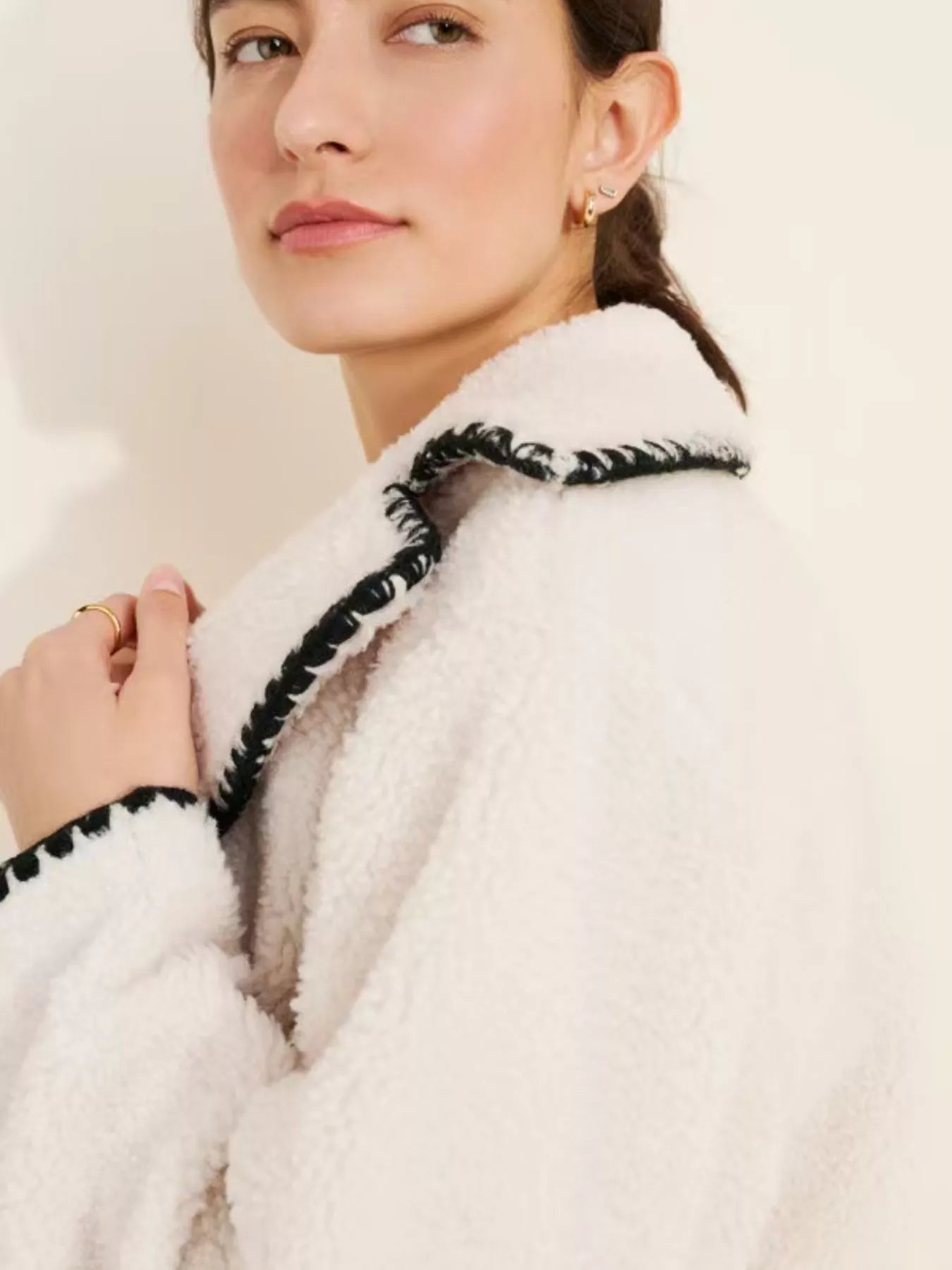NEWYORKLISTED STYLE COLLECTION: Close-up of a person wearing a white coat with black trim against a plain background