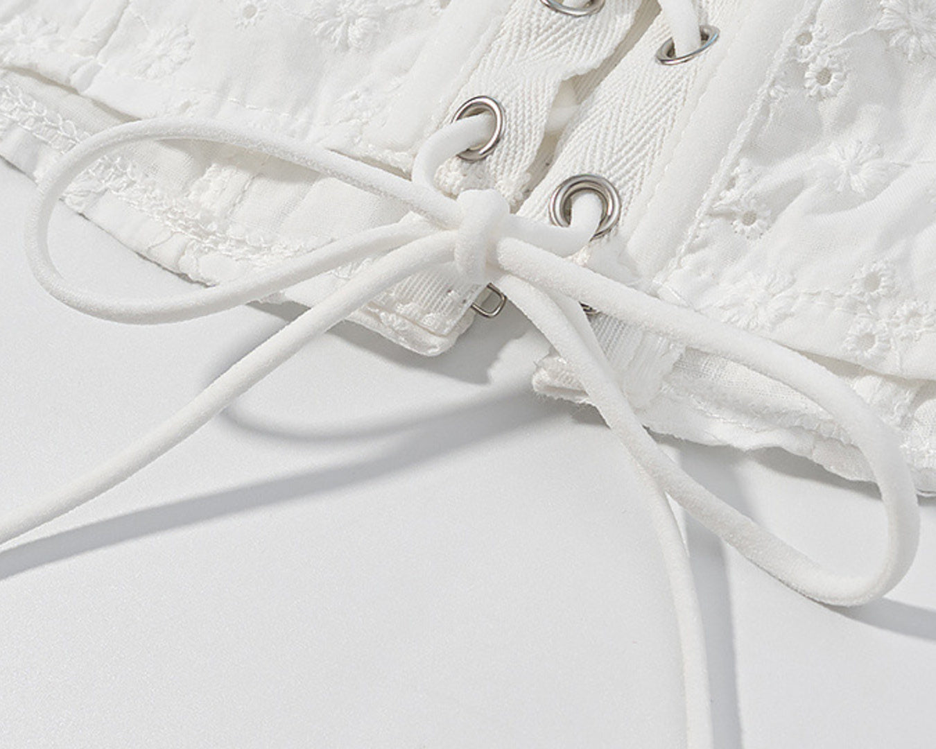 NEWYORKLISTED STYLE COLLECTION: Close-up of a white lace garment with laces on a light gray background