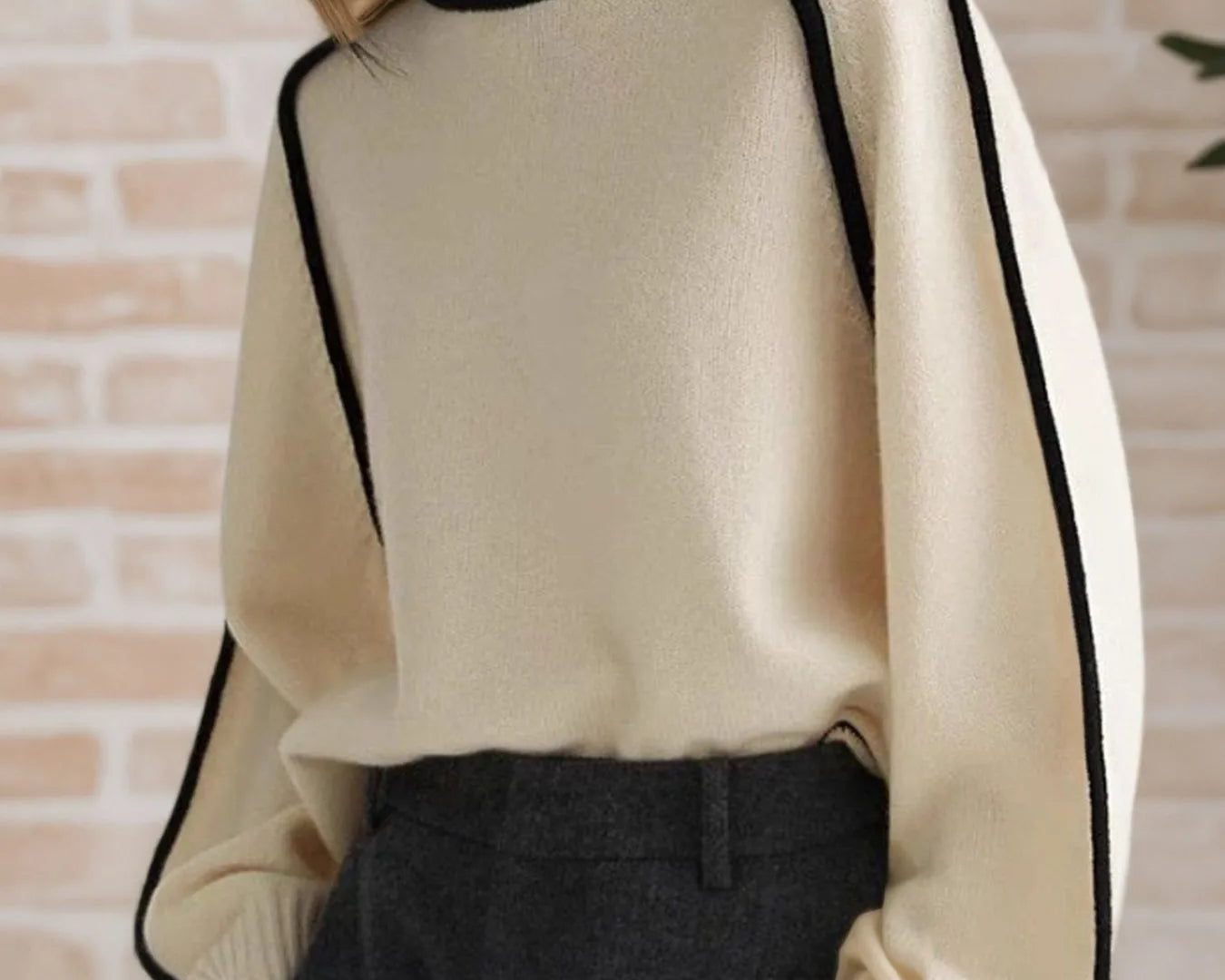 NEWYORKLISTED STYLE COLELCTION: Person wearing a cream sweater with black trim against a brick wall.