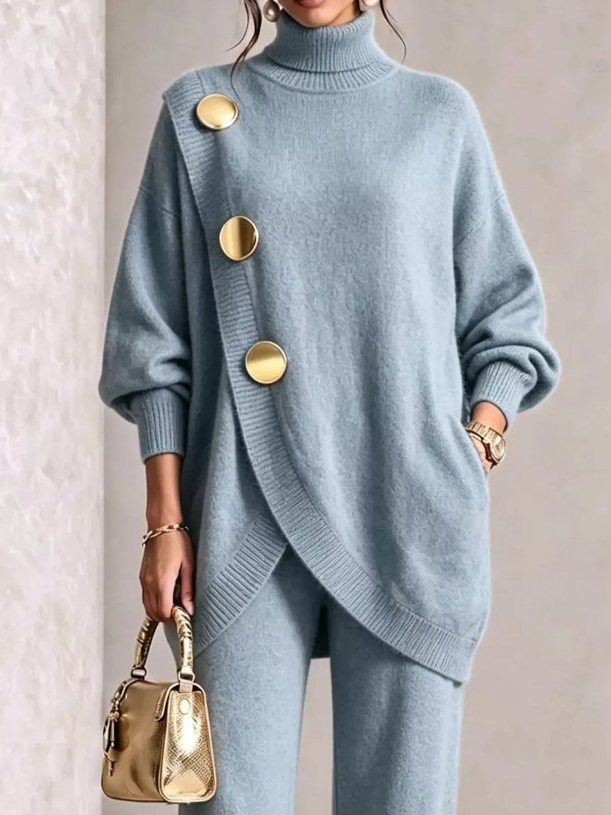 NEWYORKLISTED STYLE COLLECTION: A woman wearing a light blue knit turtleneck sweater with oversized gold buttons and matching knit pants, holding a small metallic gold handbag against a neutral indoor background.