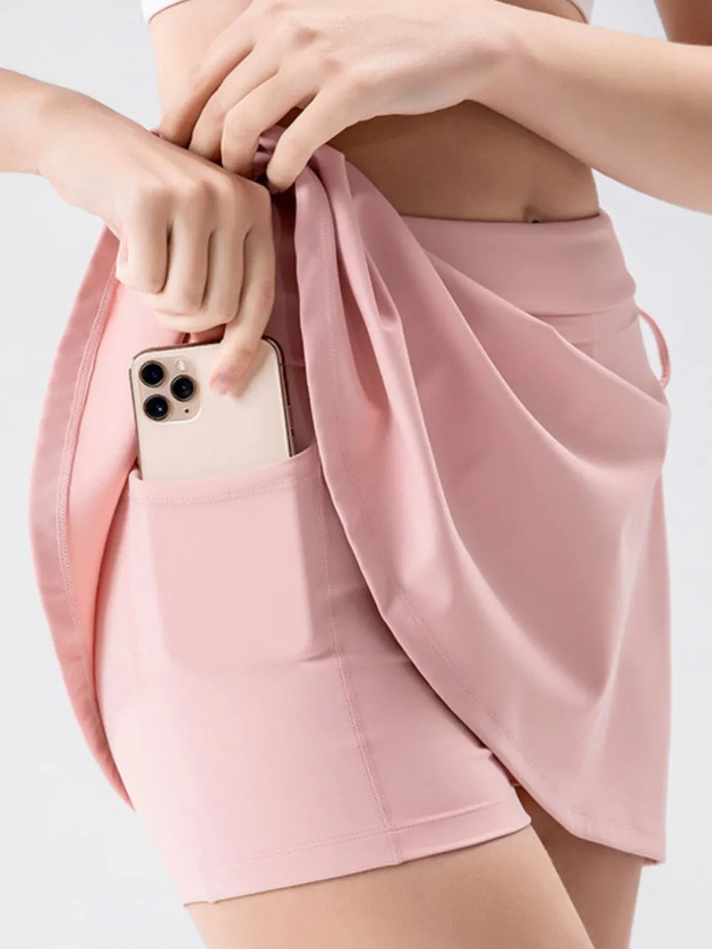 NEWYORKLISTED ACTIVEWEAR COLLECTION: Person wearing a pink skirt with a phone in the pocket on a light gray background