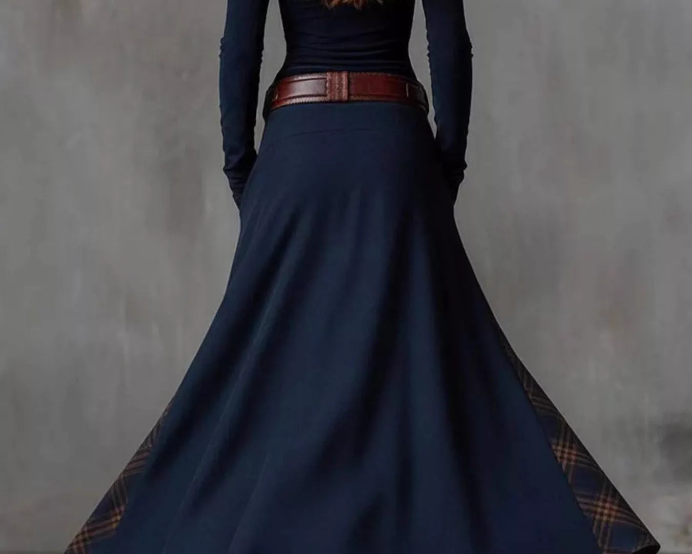 NEWYORKLISTED Style Collection: Person wearing a long navy dress with a belt and brown boots against a gray background