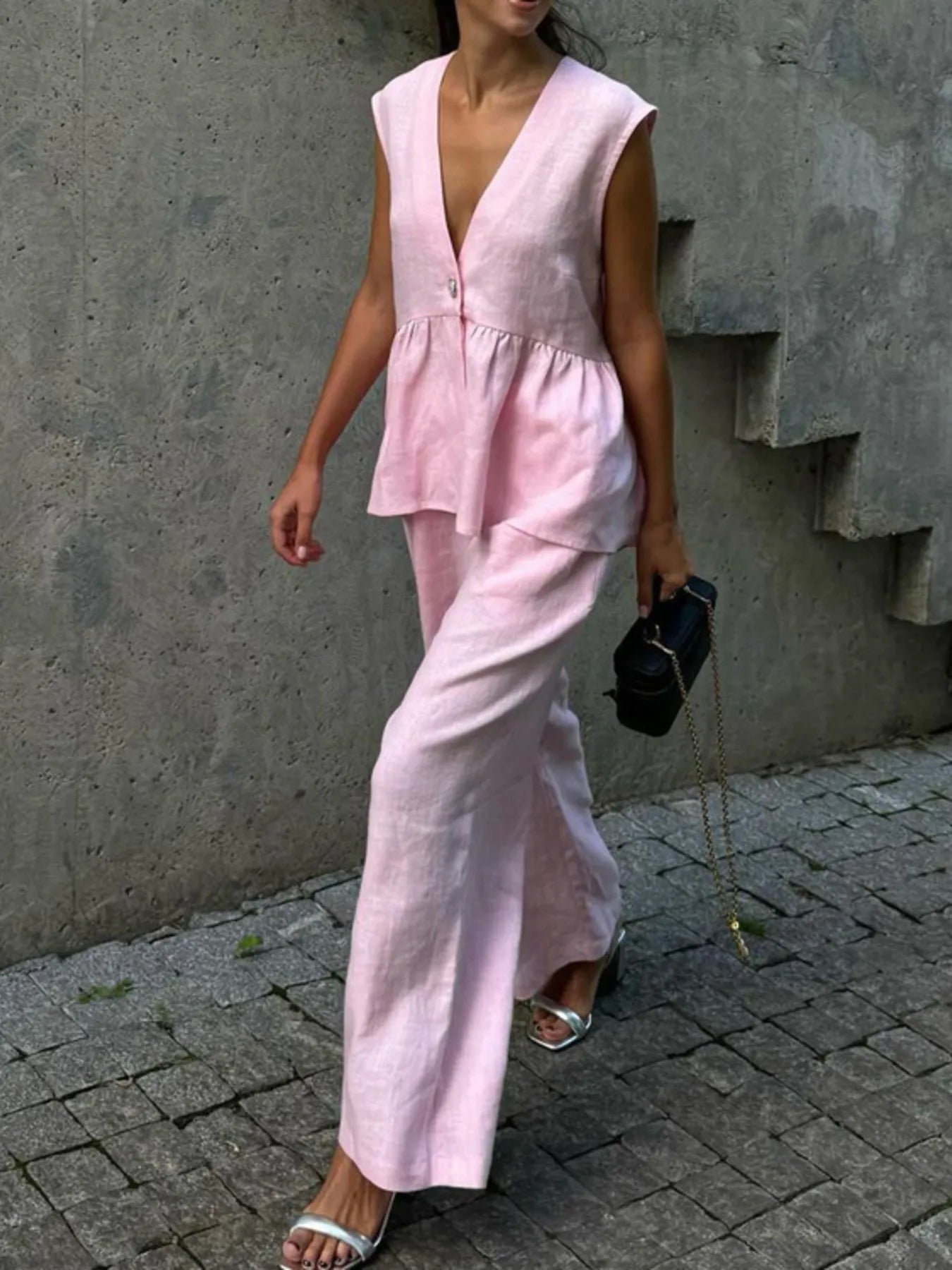 Person wearing a NEWYORKLISTED Style Model wearing pink sleeveless top and pants against a concrete wall.