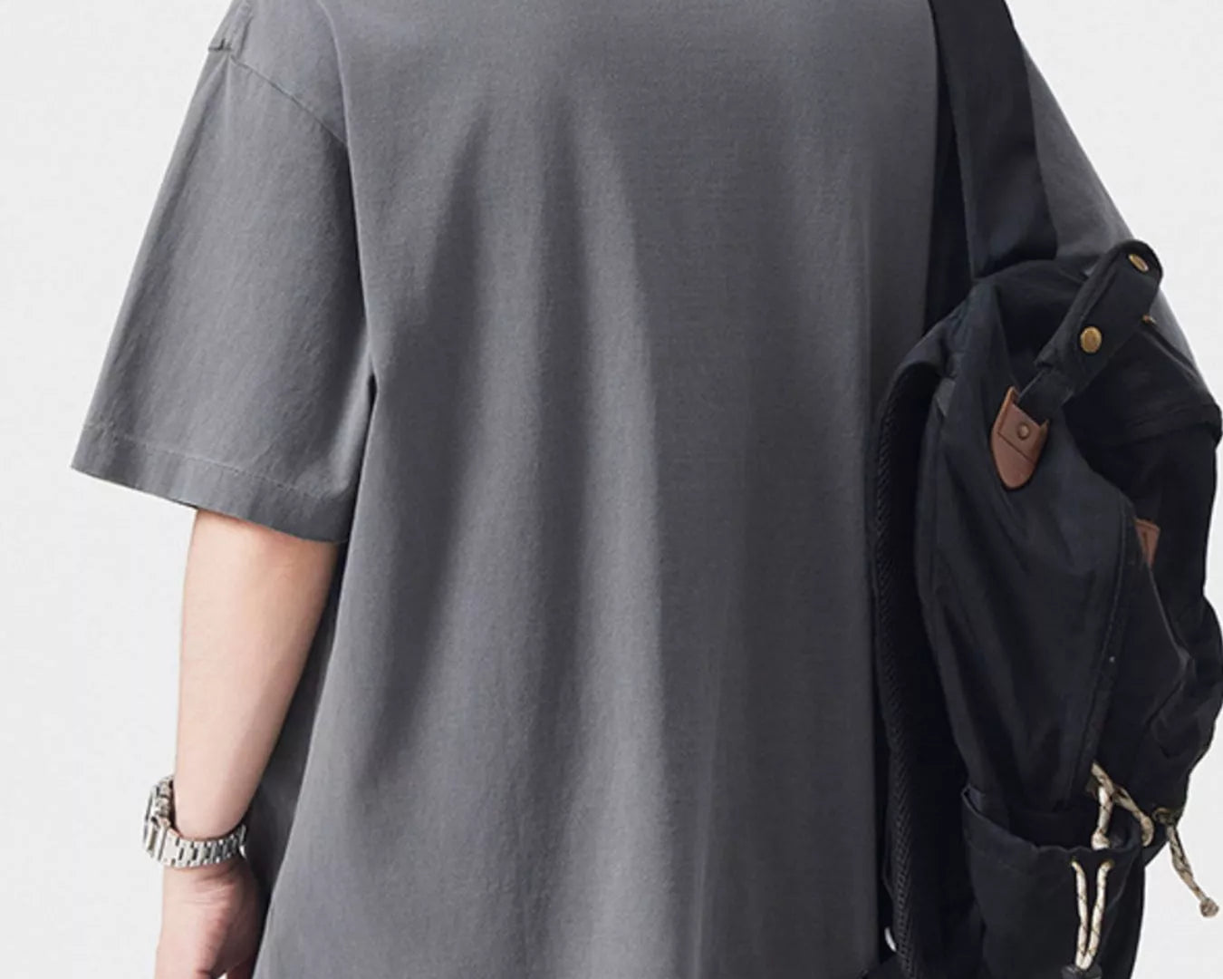 NEWYORKLISTED ATLAS MEN's COLLECTION: Person wearing a gray t-shirt and light-colored pants with a black backpack on a white background