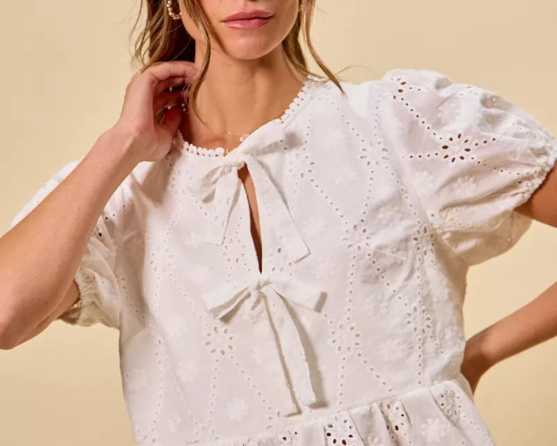 NEWYORKLISTED STYLE COLLECTION: Woman wearing a white embroidered blouse with blue jeans on a beige background