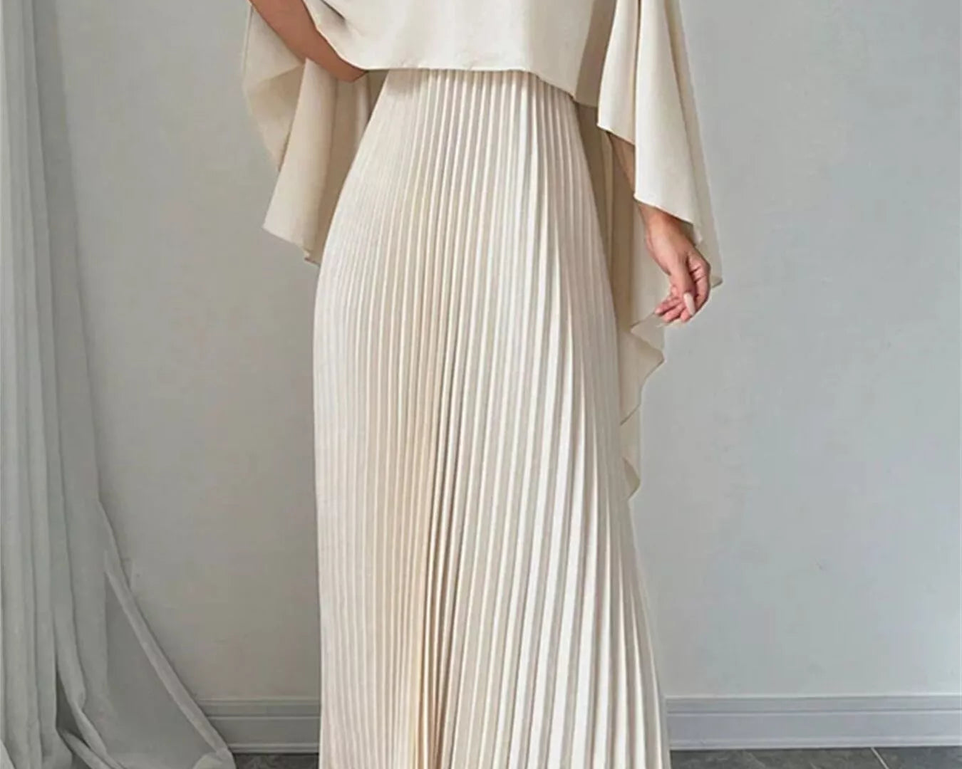NEWYORKLISTED STYLE COLLECTION: Woman wearing a long, flowing beige dress with a draped top against a plain background