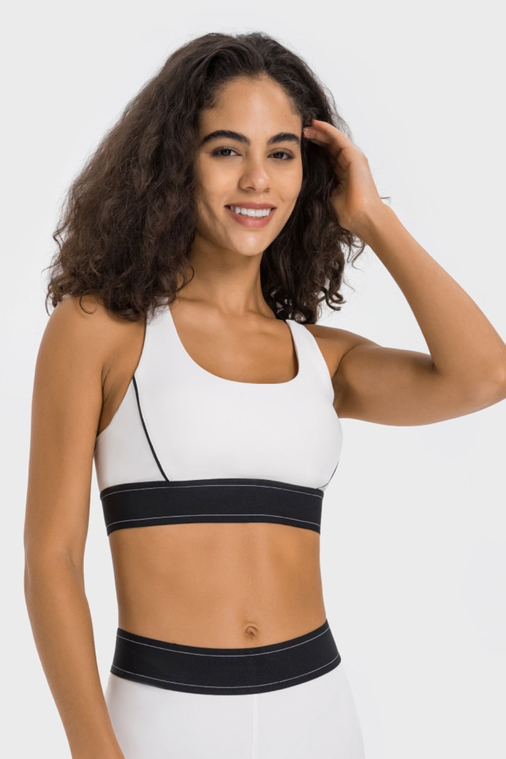 NEWYORKLISTED ACTIVEWEAR COLLECTION: Woman wearing a white sports bra with black waistband on a white background