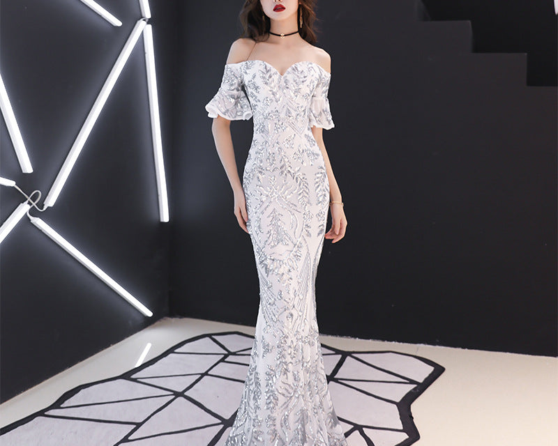 Woman in a white lace off-shoulder gown standing in a modern, geometrically lit room.