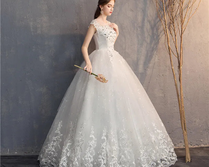 Woman in a white lace wedding dress holding a bouquet against a textured wall.