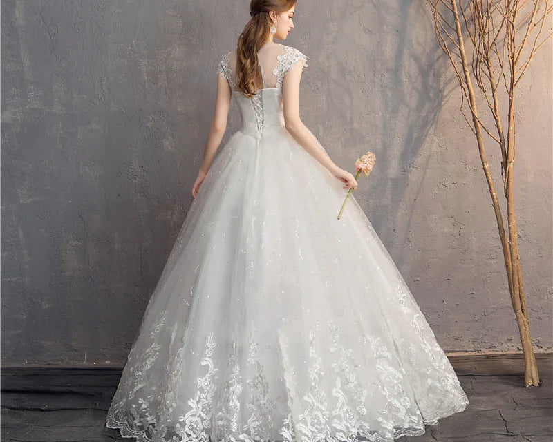 Woman in a white lace wedding dress holding a bouquet against a textured wall.