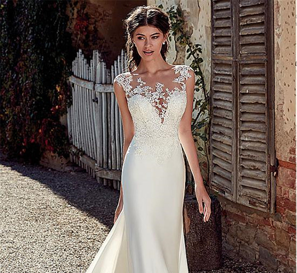 Woman in a white wedding dress standing outdoors near a rustic building.