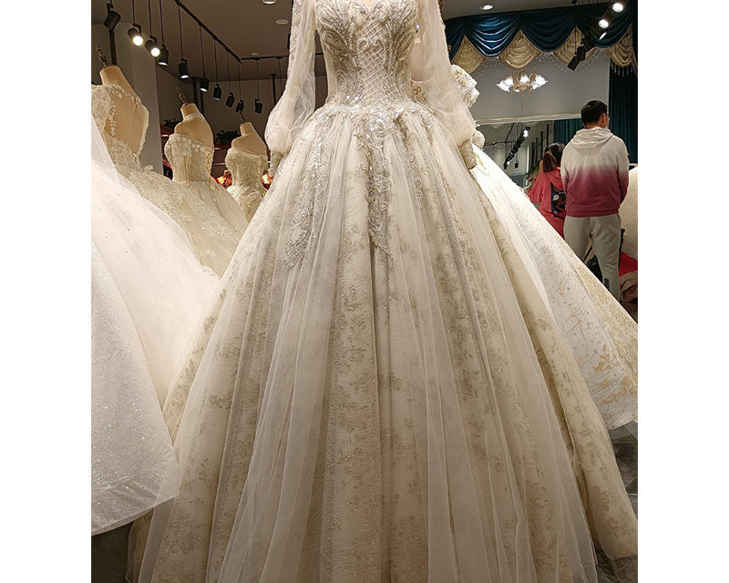 Elegant white wedding dress on a mannequin in a store setting with other dresses and people in the background.
