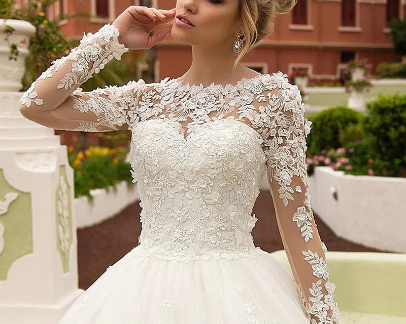 NEWYORKLISTED ELEGANT BRIDE COLLECTION: Woman wearing a white lace wedding dress with long sleeves in an outdoor setting.