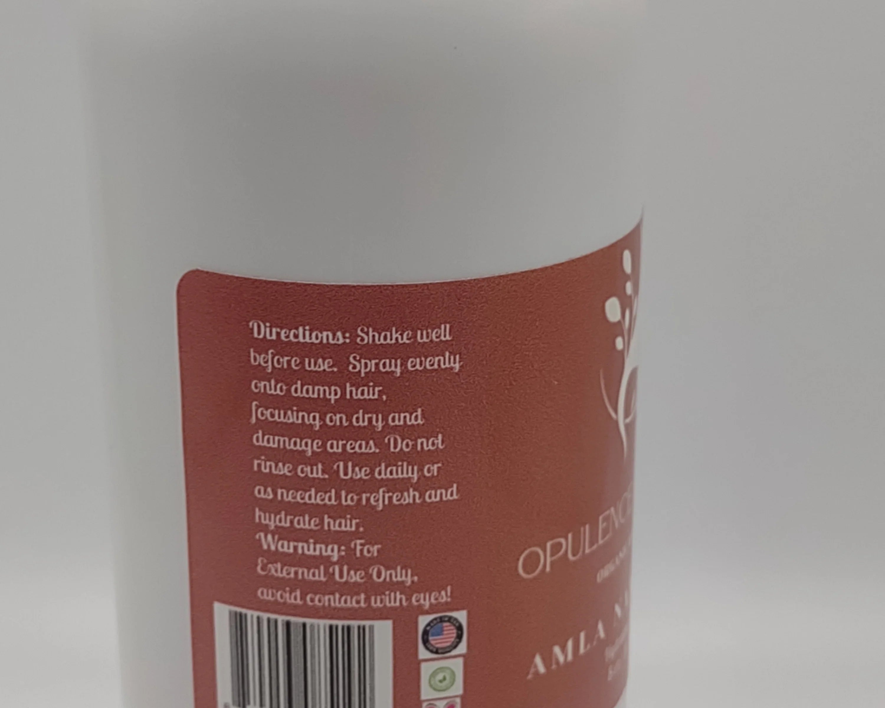 Close-up of a bottle label with text and a barcode on a white background: AMLA NATURALS - Opulent Hair Nourishment Mist