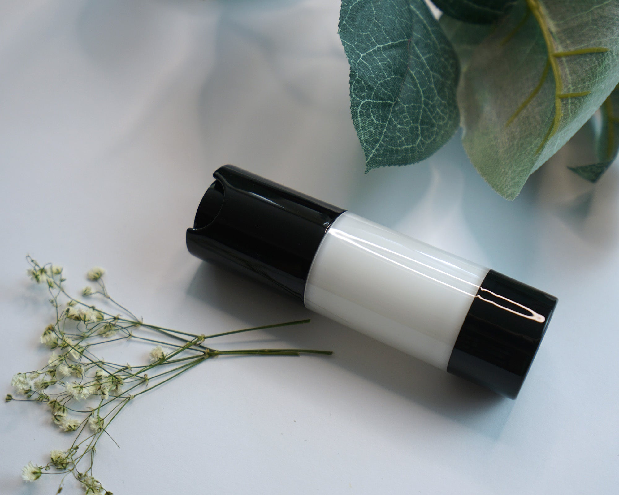 NEWYORKLISTED COSMETIC COLLECTION: Extreme Moisture Blend: bottle with black cap and white body on a light surface with green leaves and flowers.