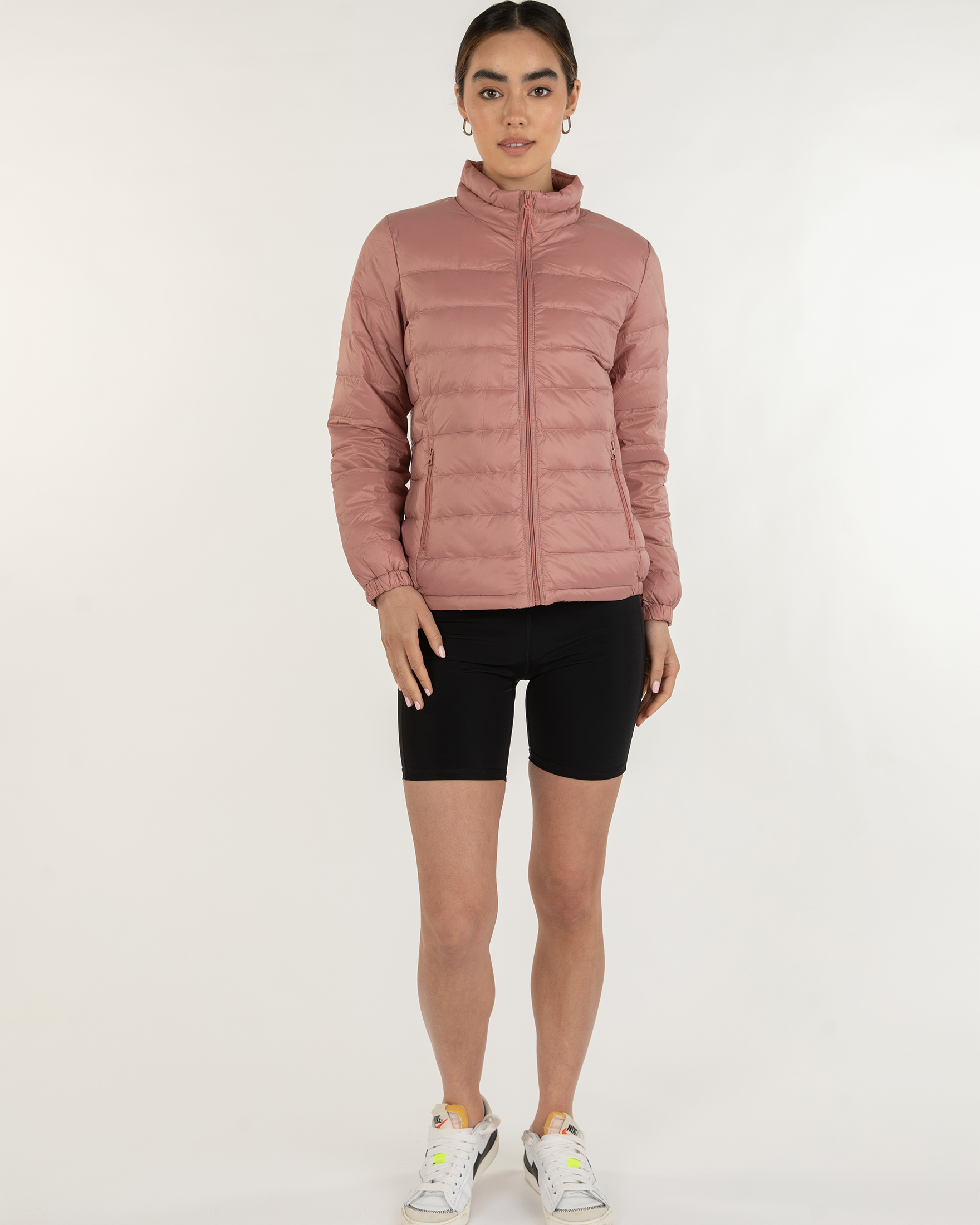 Person wearing a pink puffer jacket and black shorts on a white background