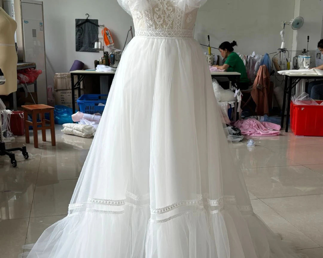 White lace wedding dress on a mannequin in a workshop setting.