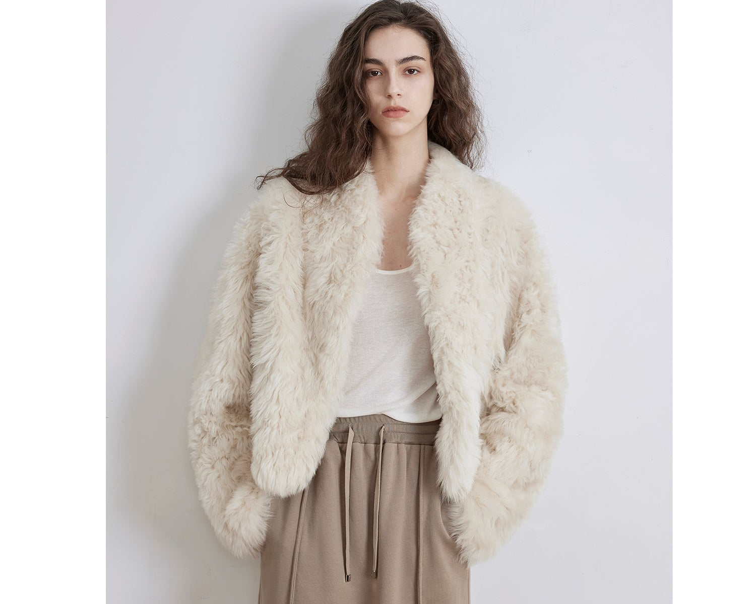 NEWYORKLISTED STYLE COLLECTION: Woman wearing a fluffy white jacket over a white shirt and beige pants on a light gray background