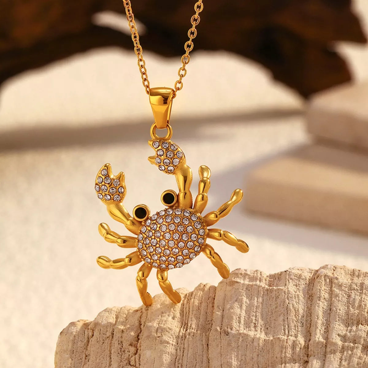 NYLD Glamour Collection by NEWYORKLISTED: Gold crab-shaped pendant necklace on a wooden surface