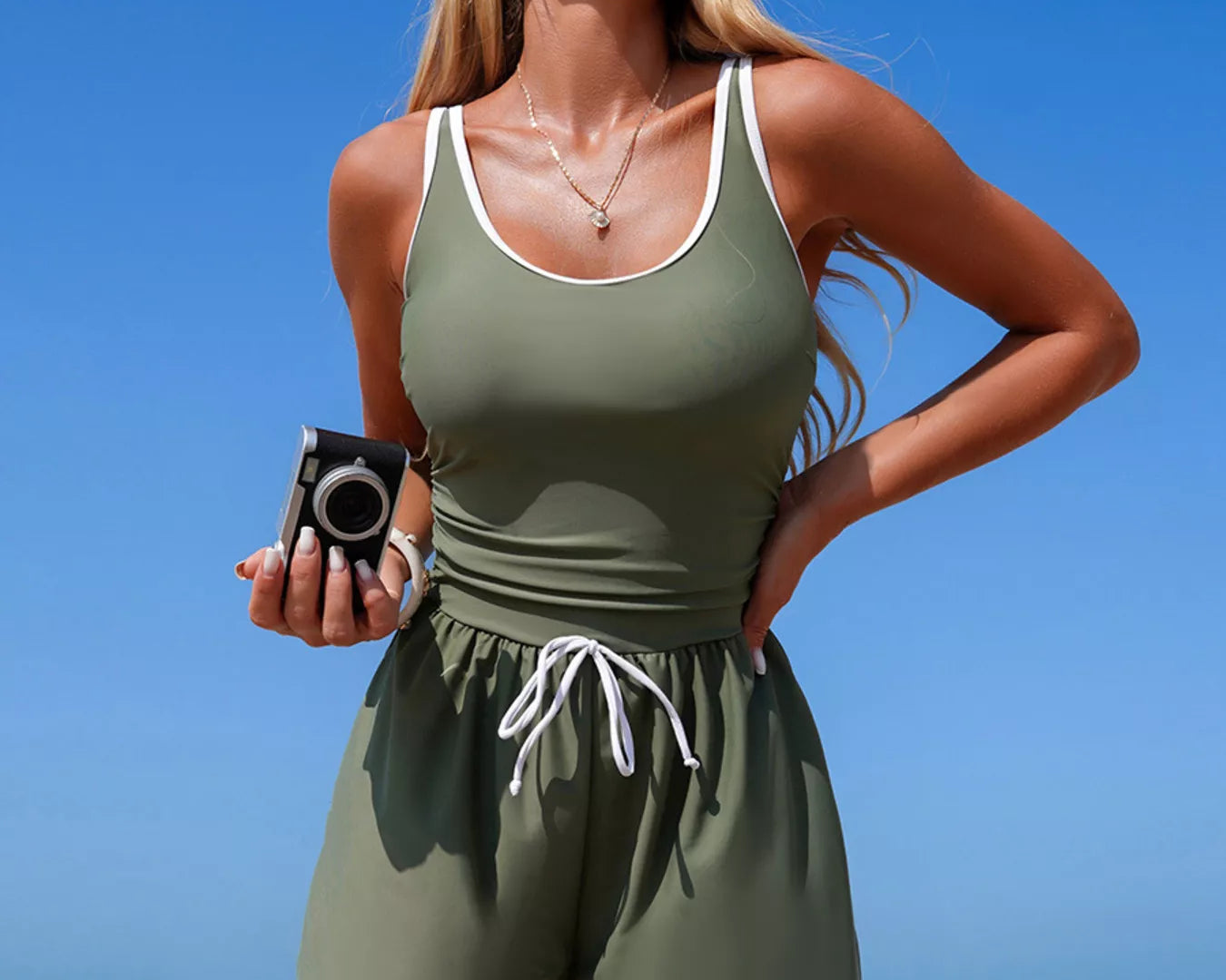 NEWYORKLISTED STYLE COLLECTION: Woman in green athletic outfit standing on a beach with clear blue sky