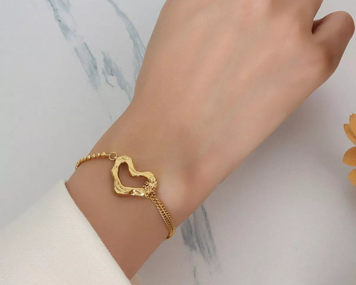 NYLD Glamour Collection by NEWYORKLISTED: Gold bracelet with a heart design on a wrist against a marble background