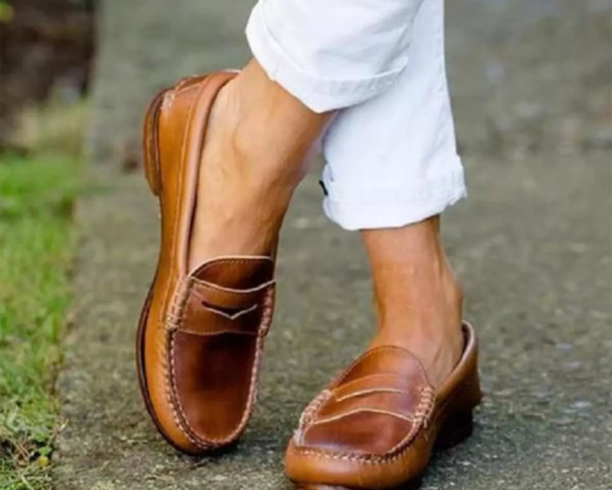 NEWYORKLISTED SHOE COLLECTION: Brown loafers worn with white pants on a blurred outdoor background