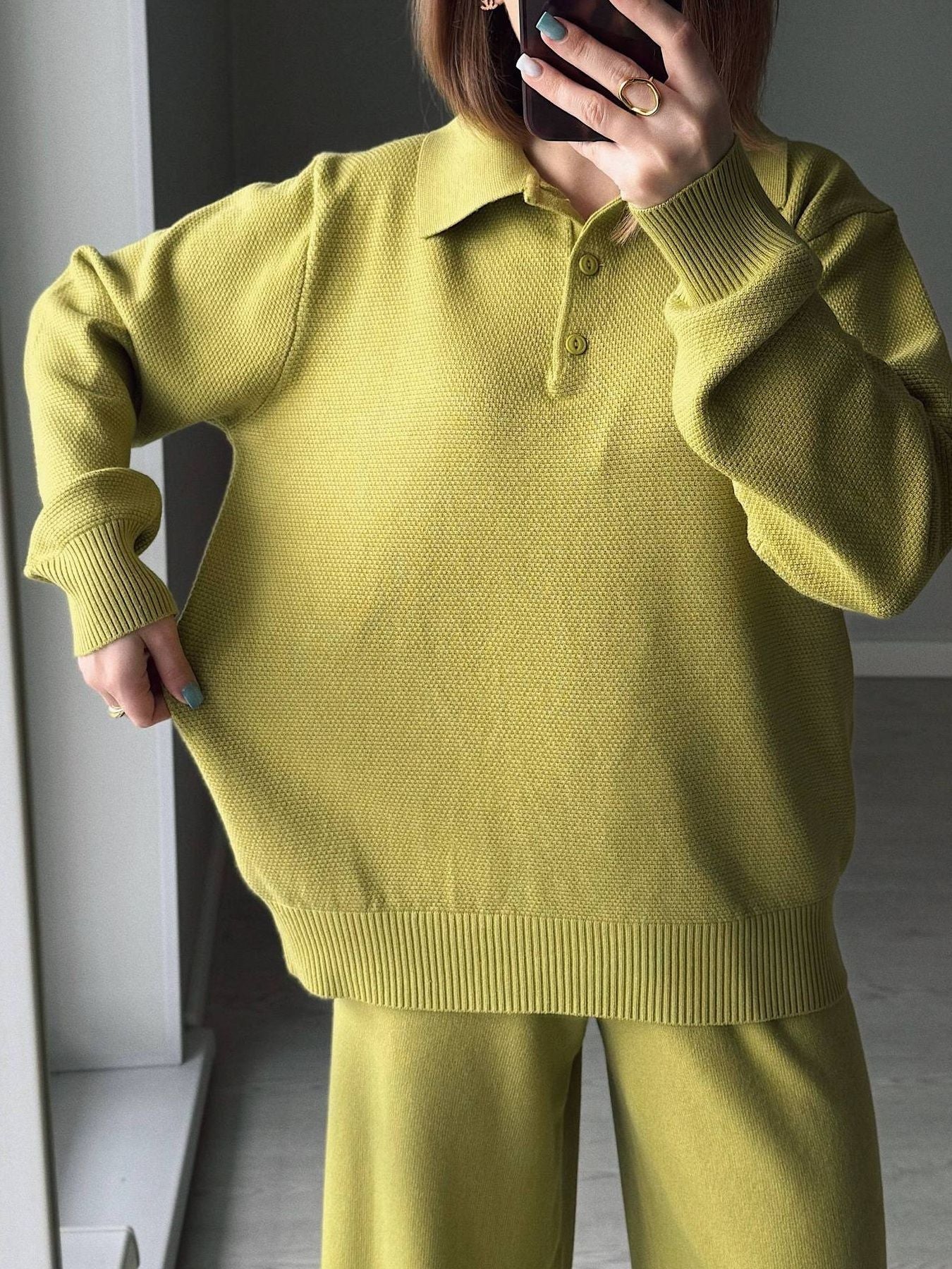 Person wearing a green sweater and pants taking a mirror selfie.