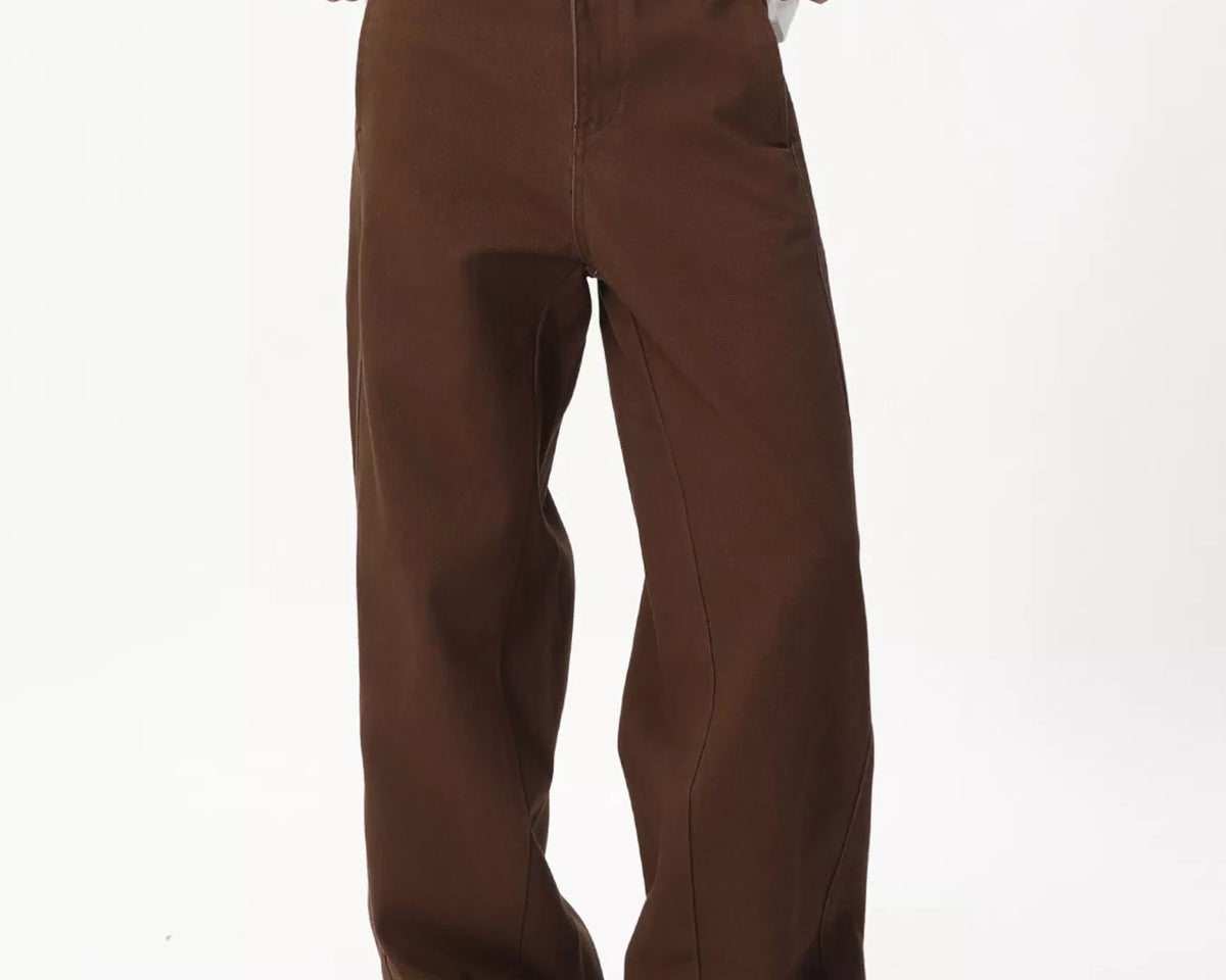 NEWYORKLISTED ATLAS MEN'S COLLECTION: A person wearing loose-fit brown wide-leg pants, styled with a white graphic t-shirt and beige slip-on shoes, photographed against a plain white studio background.