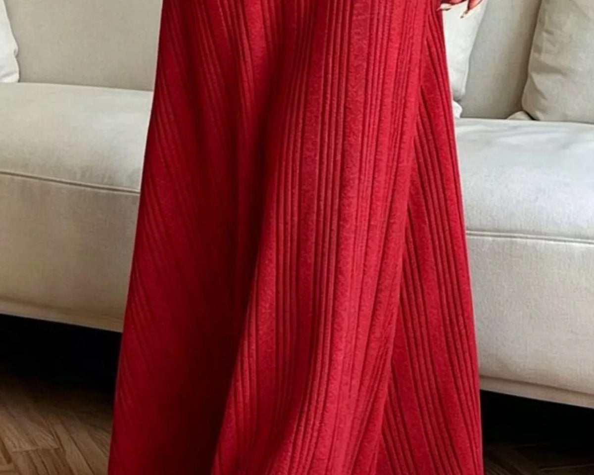 NEWYORKLISTED STYLE COLLECTION: A person wearing a long-sleeve, floor-length red ribbed knit dress standing in front of a light beige sofa on a wood floor.