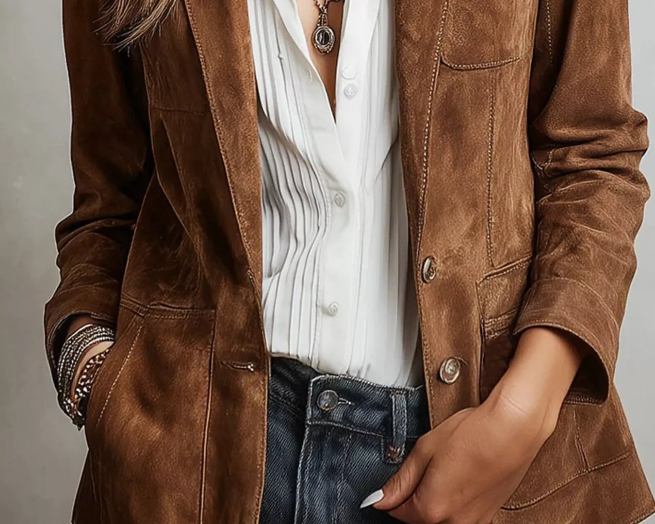 NEWYORKLISTED STYLE COLLECTION: Person wearing a brown suede jacket over a white shirt and blue jeans on a neutral background