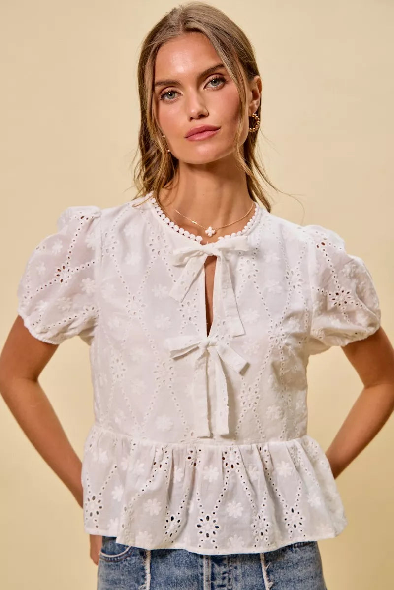NEWYORKLISTED STYLE COLLECTION: Woman wearing a white embroidered blouse with puffed sleeves on a beige background